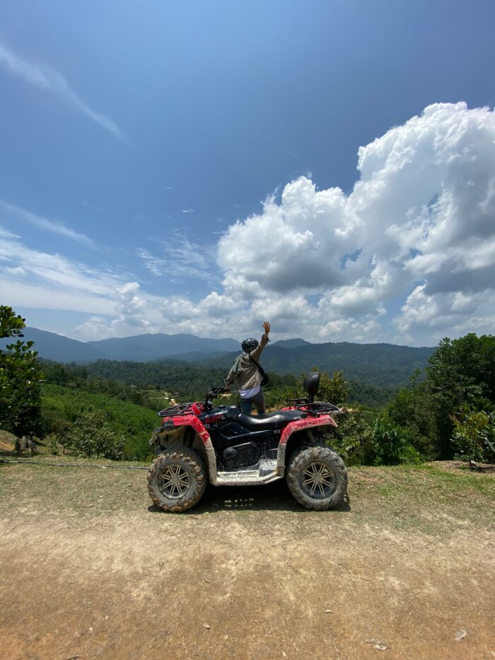 Person standing triumphantly on a 4-wheeler, overlooking beautiful green landscape and blue skies