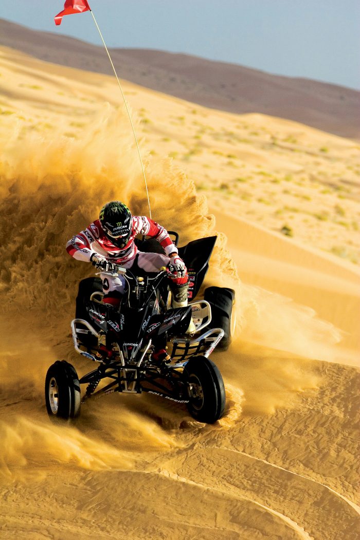 Person driving an ATV through a desert landscape, leaving a cloud of dust behind them